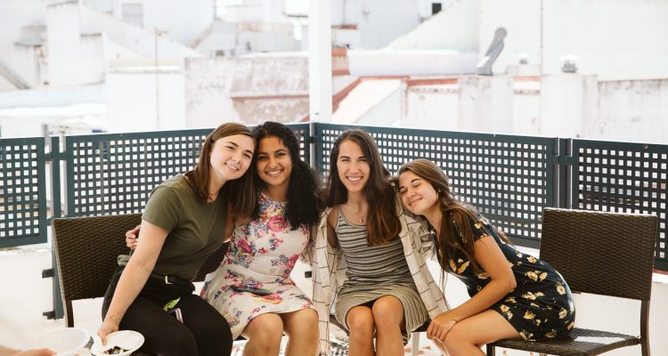 Diverse group of women sitting on a bench smiling.